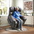 Woman sitting in a recliner chair in a home setting with a window and dresser in the background.