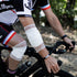 Cyclist wearing protective white knee and elbow pads on a bike.