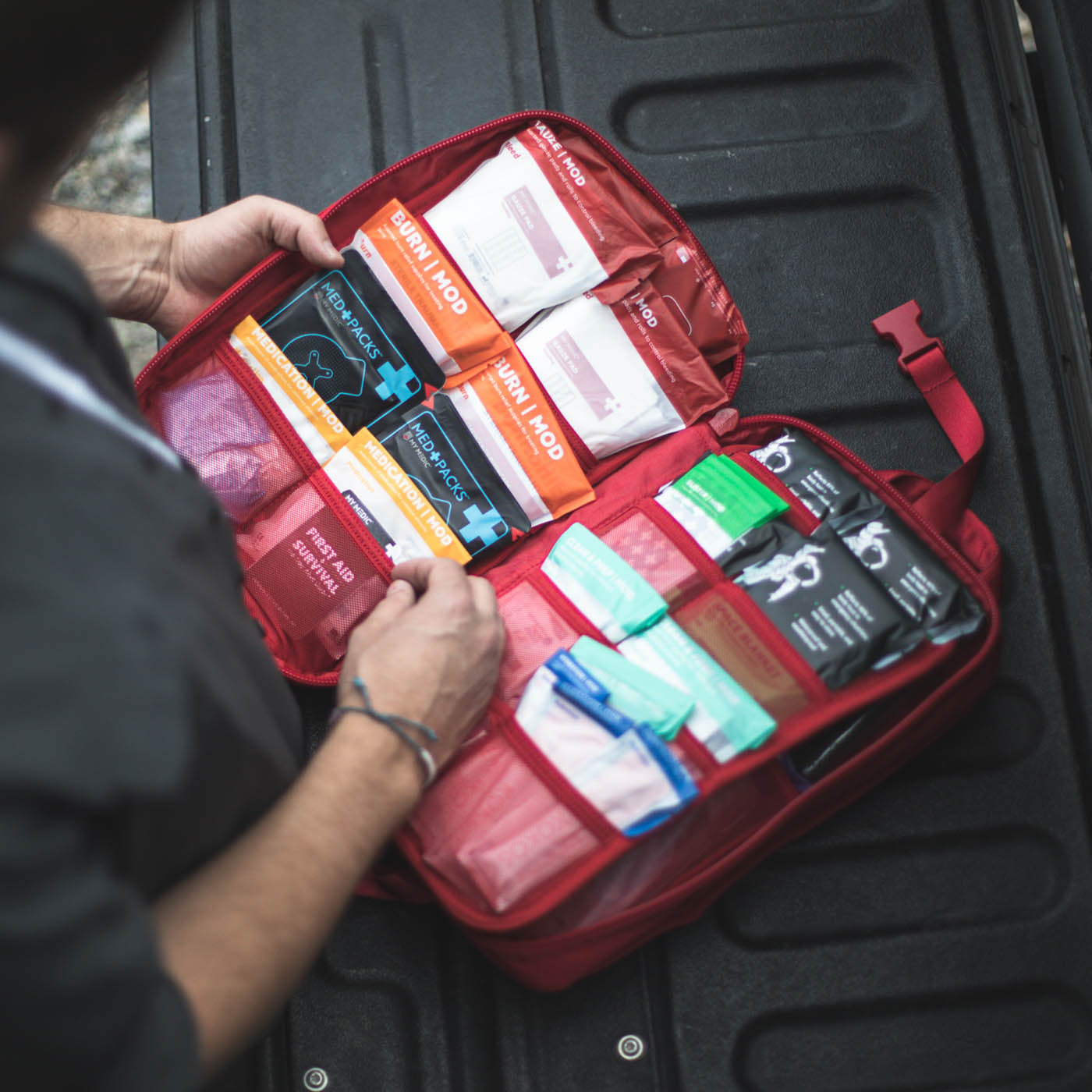 First aid kit with various supplies inside a red case held by a person.