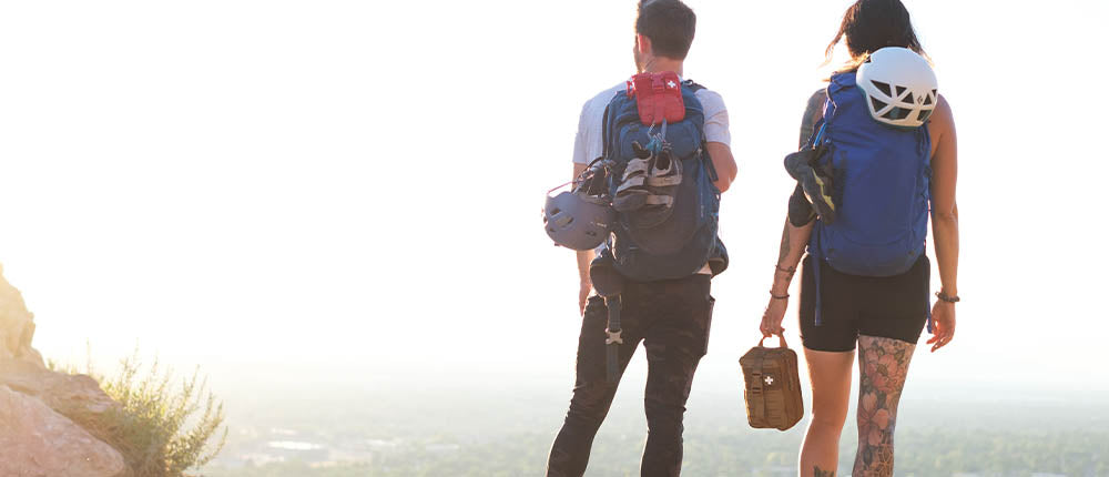 Two people with backpacks walking on a beach with a bright light source in the background