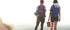 Two people with backpacks walking on a beach with a bright light source in the background